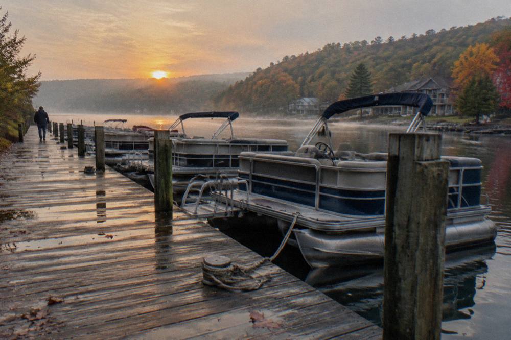 Rental pontoon boats tied along a wooden dock on a calm lake morning
